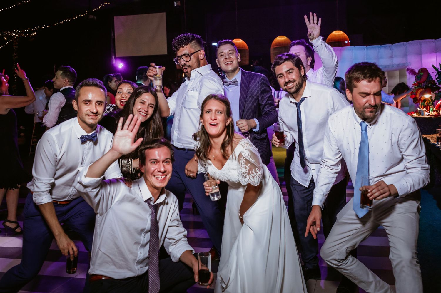 Bride surrounded by celebrating wedding guests posing together at lively indoor reception party.