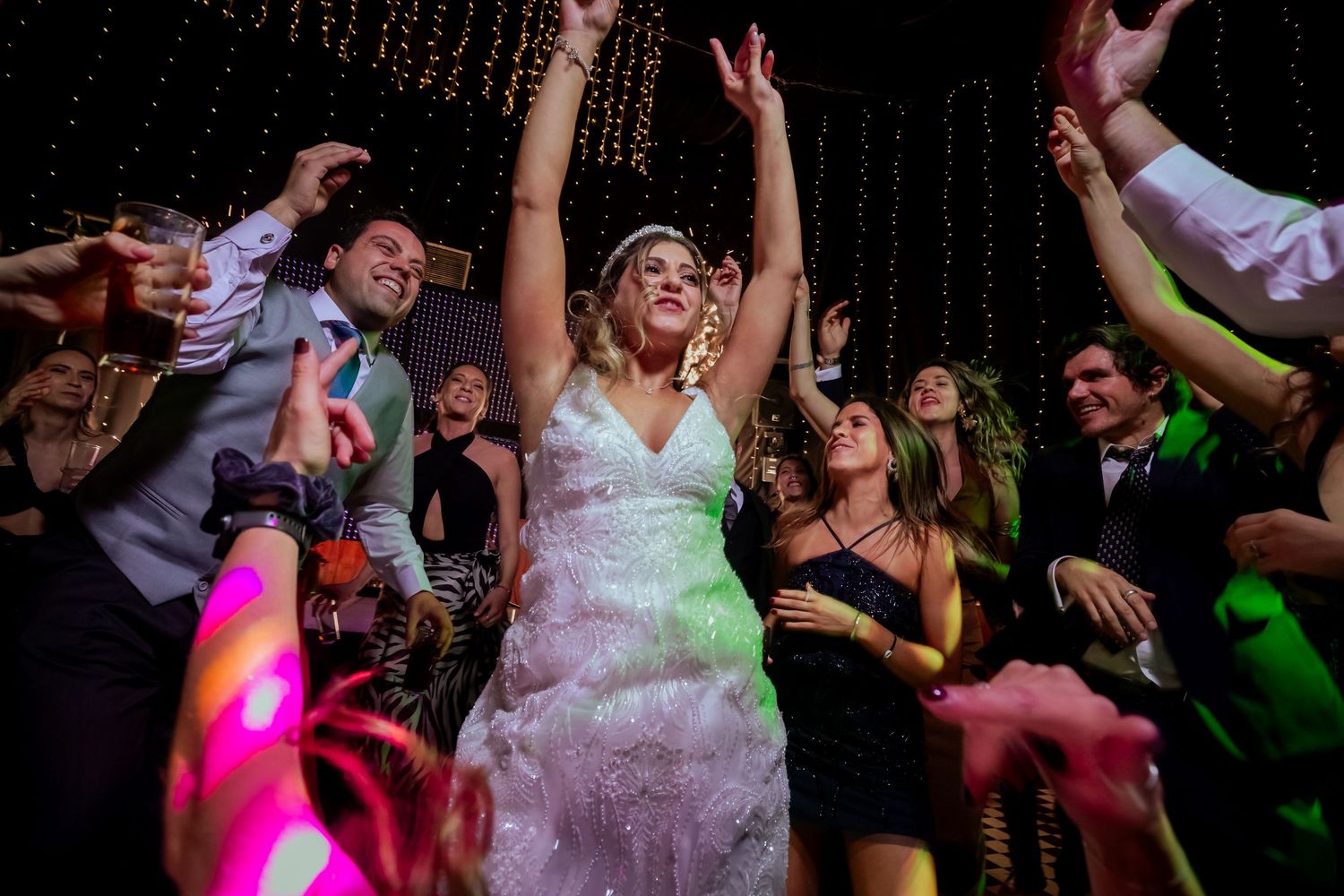Bride dances with hands raised surrounded by cheering guests at a vibrant wedding celebration.