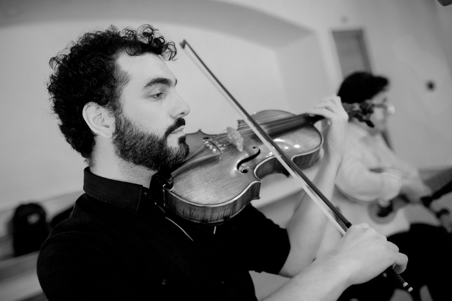 Bearded male violinist performing passionately in black and white wedding ceremony photo.