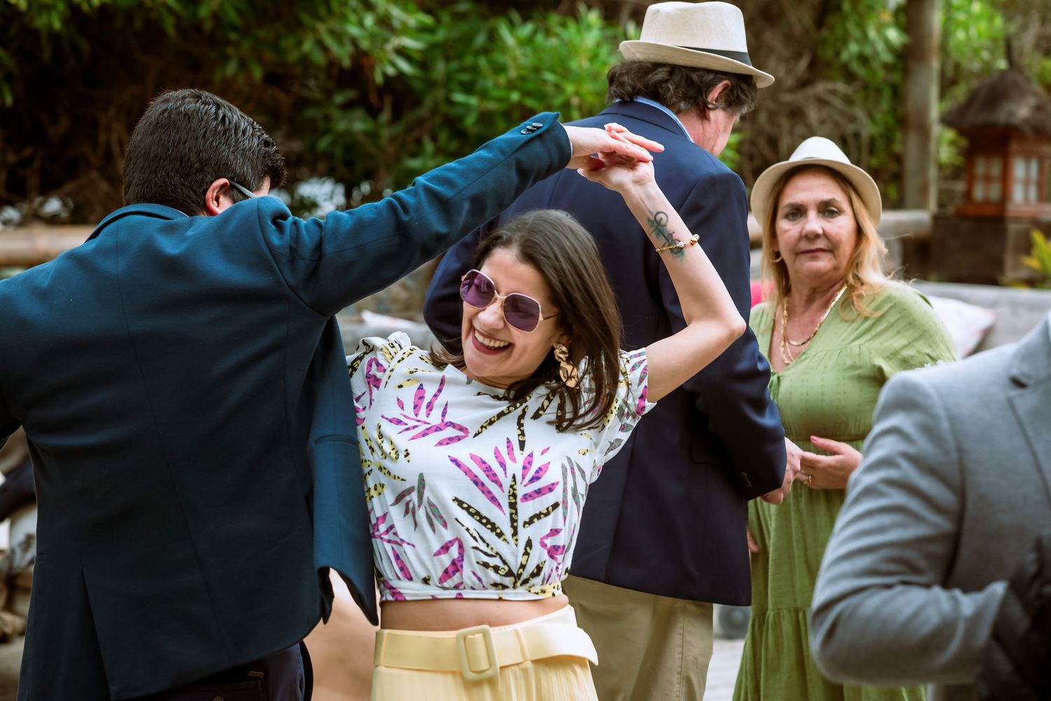 Woman in floral top dancing with sunglasses at an outdoor wedding reception with guests.