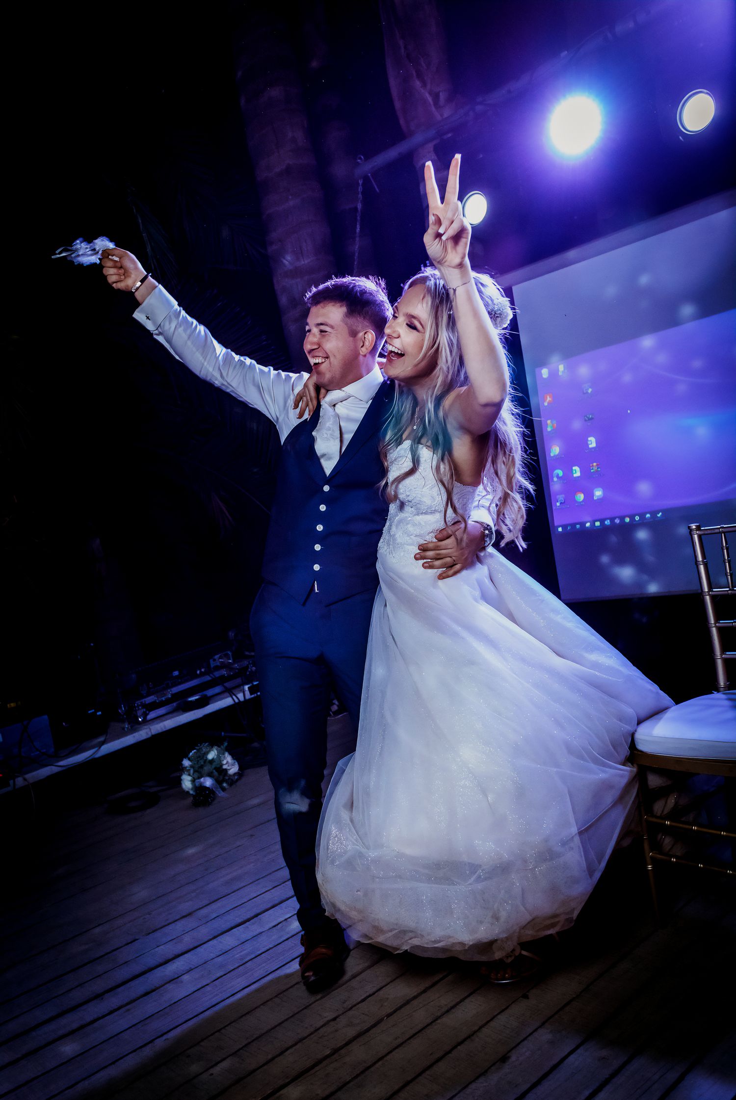 Bride and groom celebrating joyfully on stage with peace signs at their vibrant wedding reception.