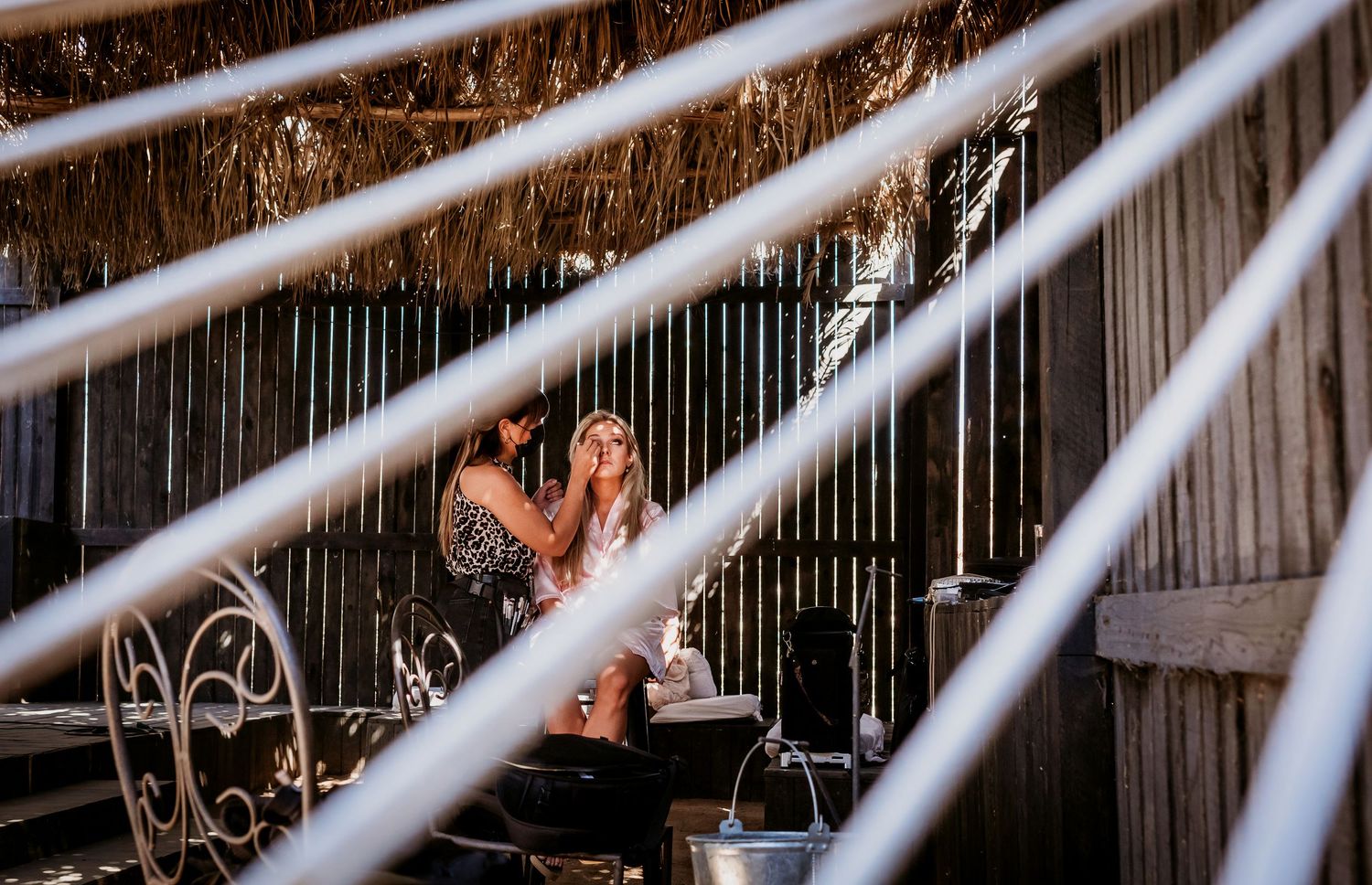A blonde woman sits in a rustic barn setting, photographed through diagonal lines creating a dramatic framing effect.