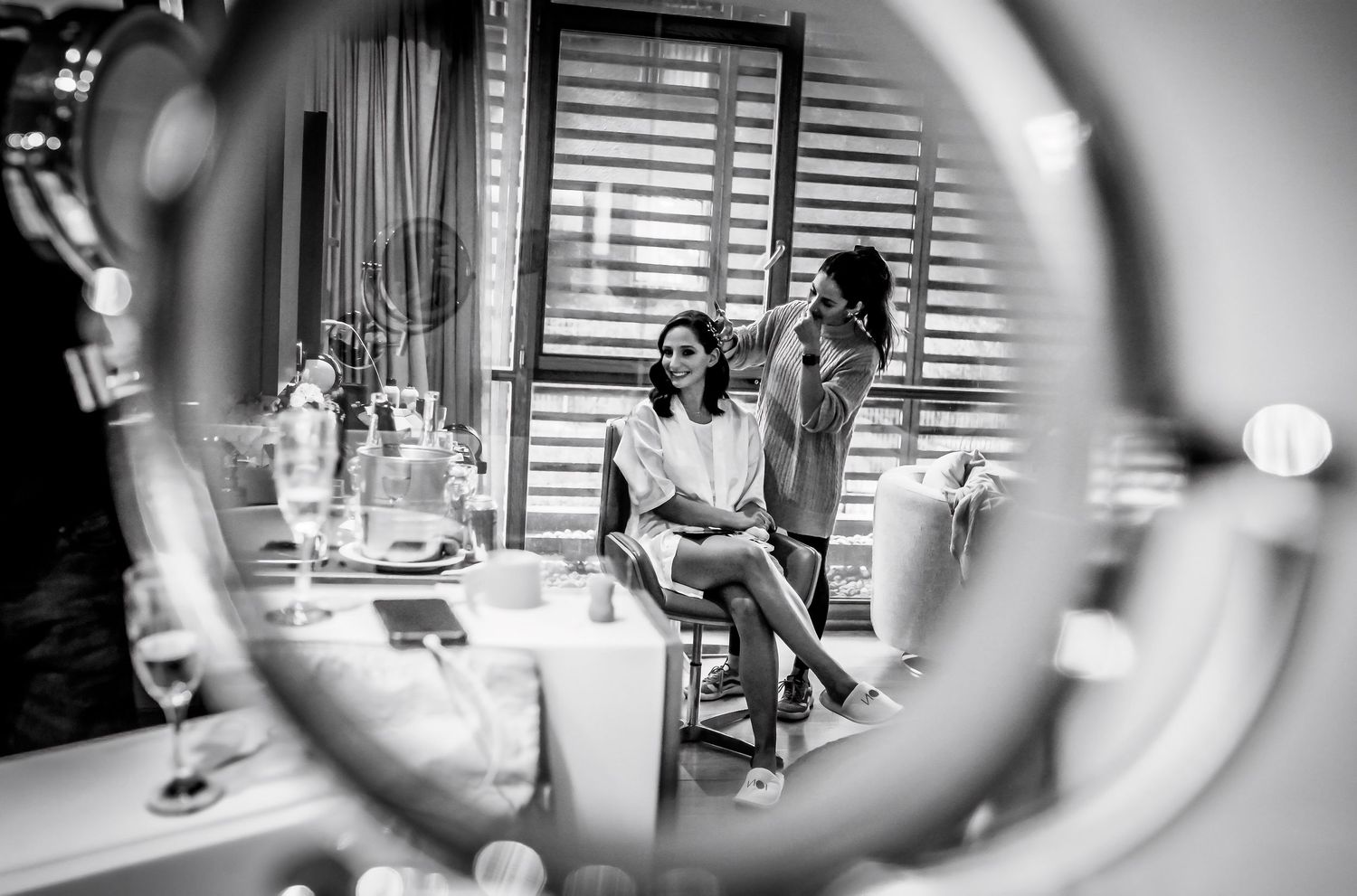 Black and white photo of two women chatting in an elegant room, reflected in a vanity mirror.