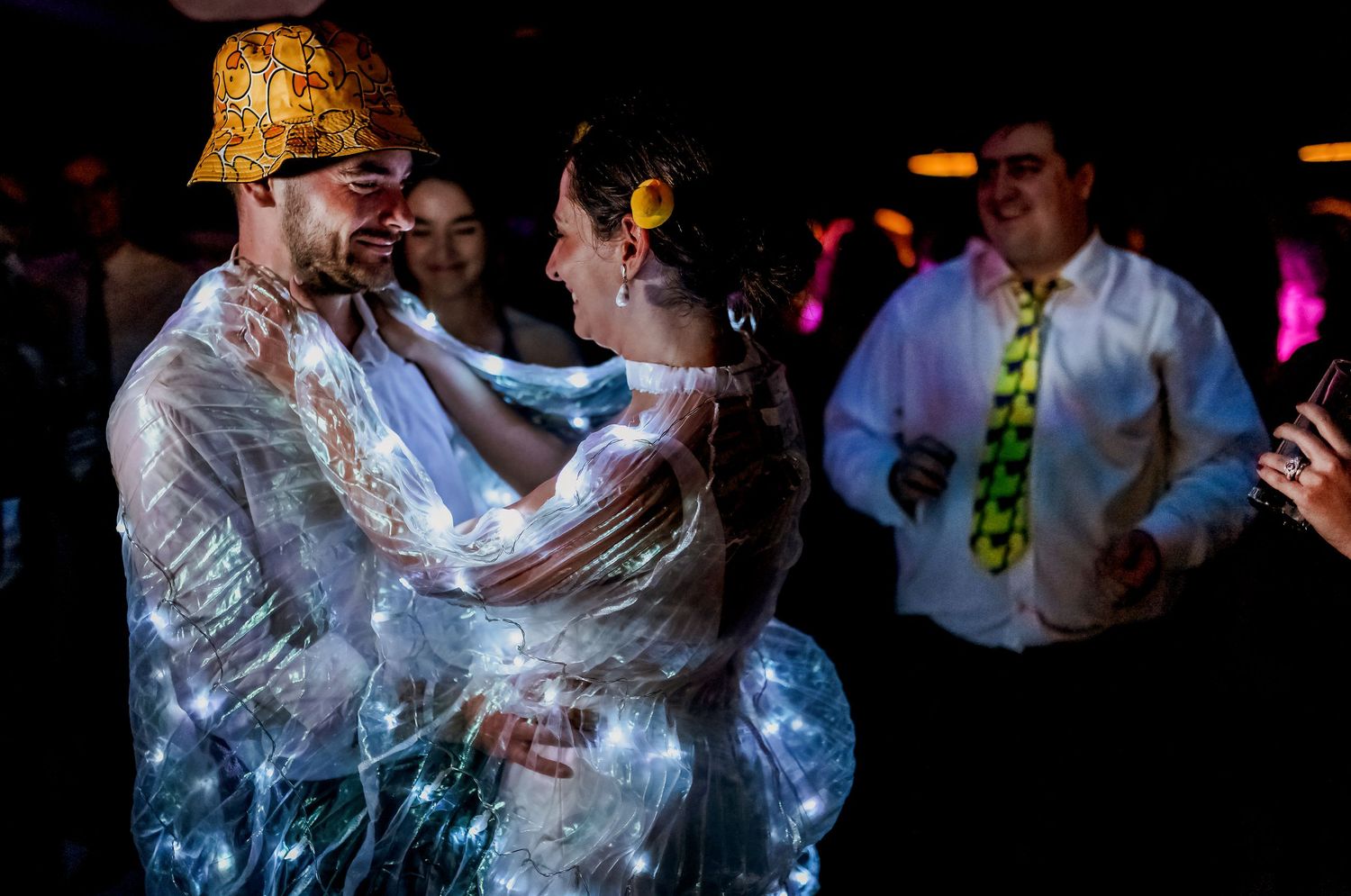 Couple dancing in illuminated LED outfits at a wedding reception party.