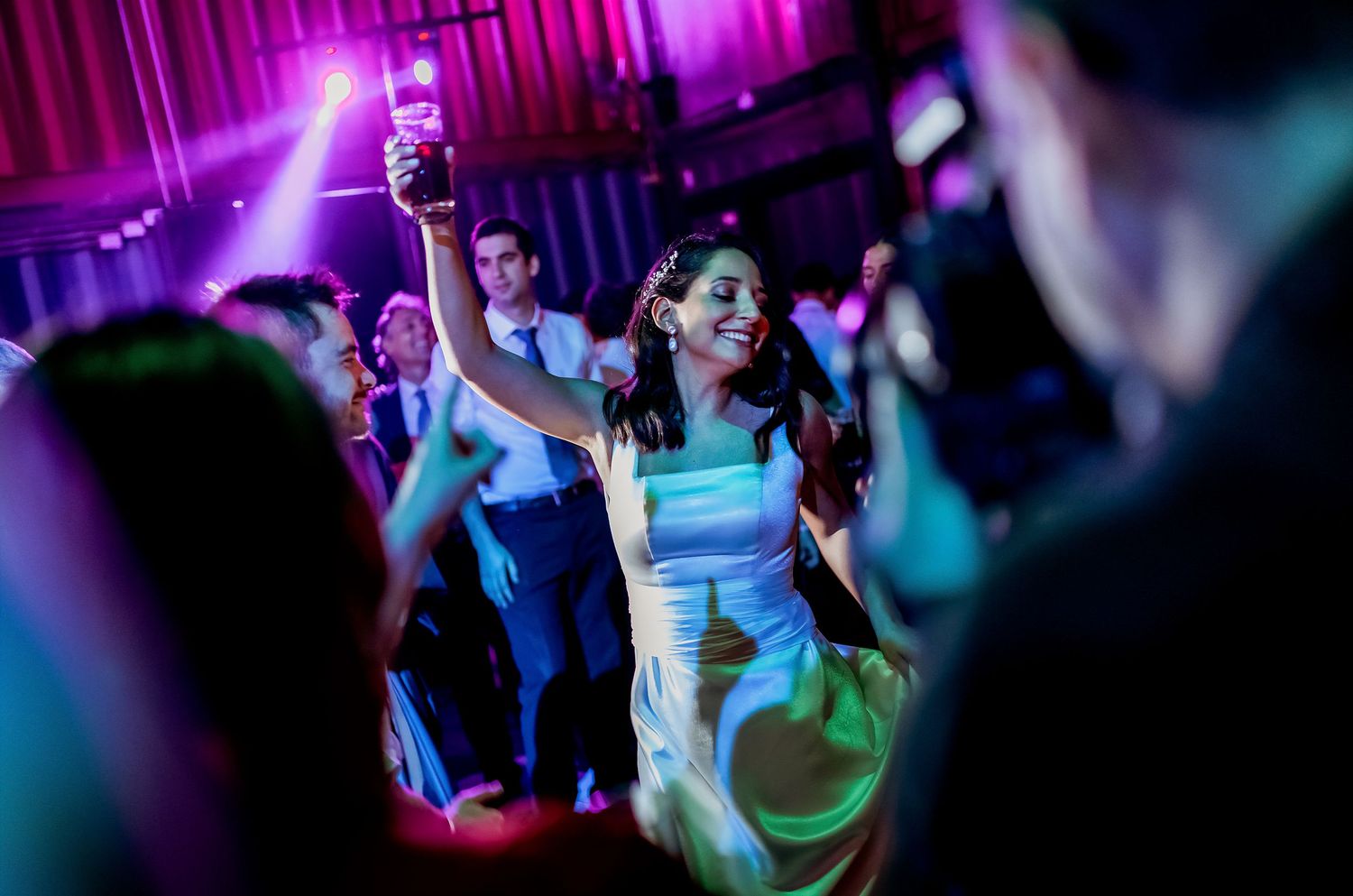 Woman in elegant dress dancing joyfully at a vibrant wedding reception with colorful lights.