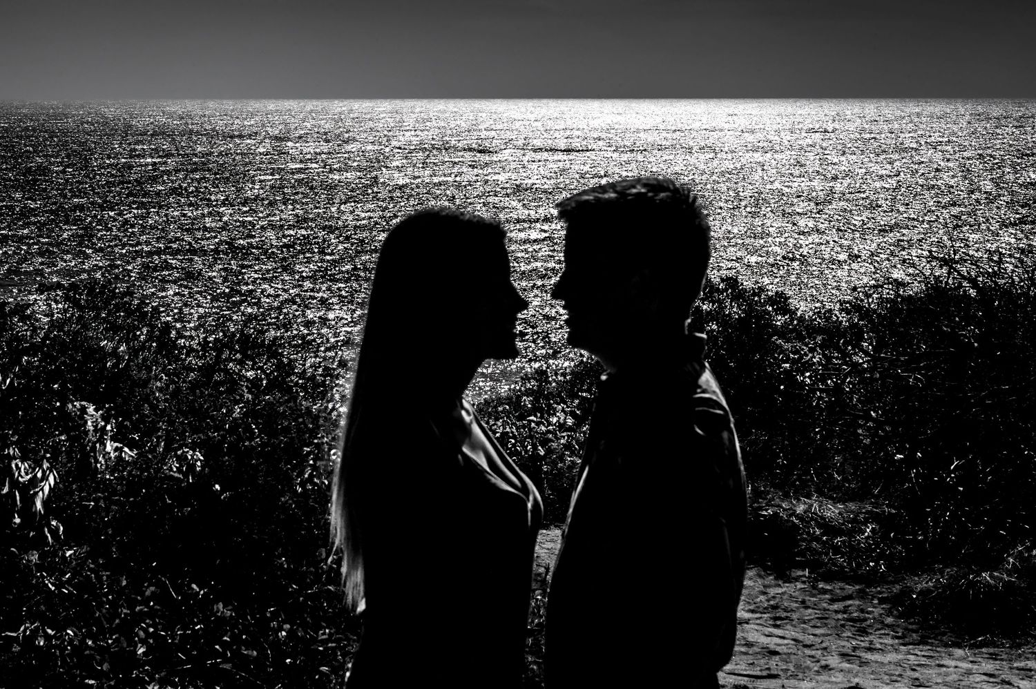 Romantic silhouette of a couple facing each other with sparkling ocean water in the background.