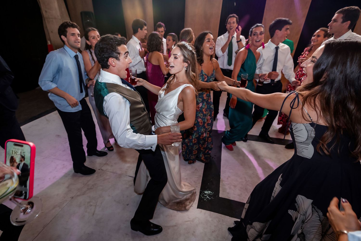 Bride and groom dancing energetically with wedding guests on a lively reception dance floor.