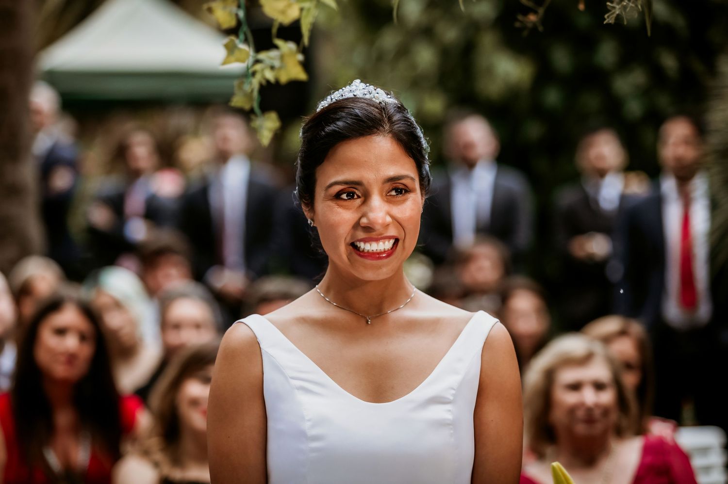 Smiling bride wearing a tiara poses during her outdoor garden wedding ceremony.