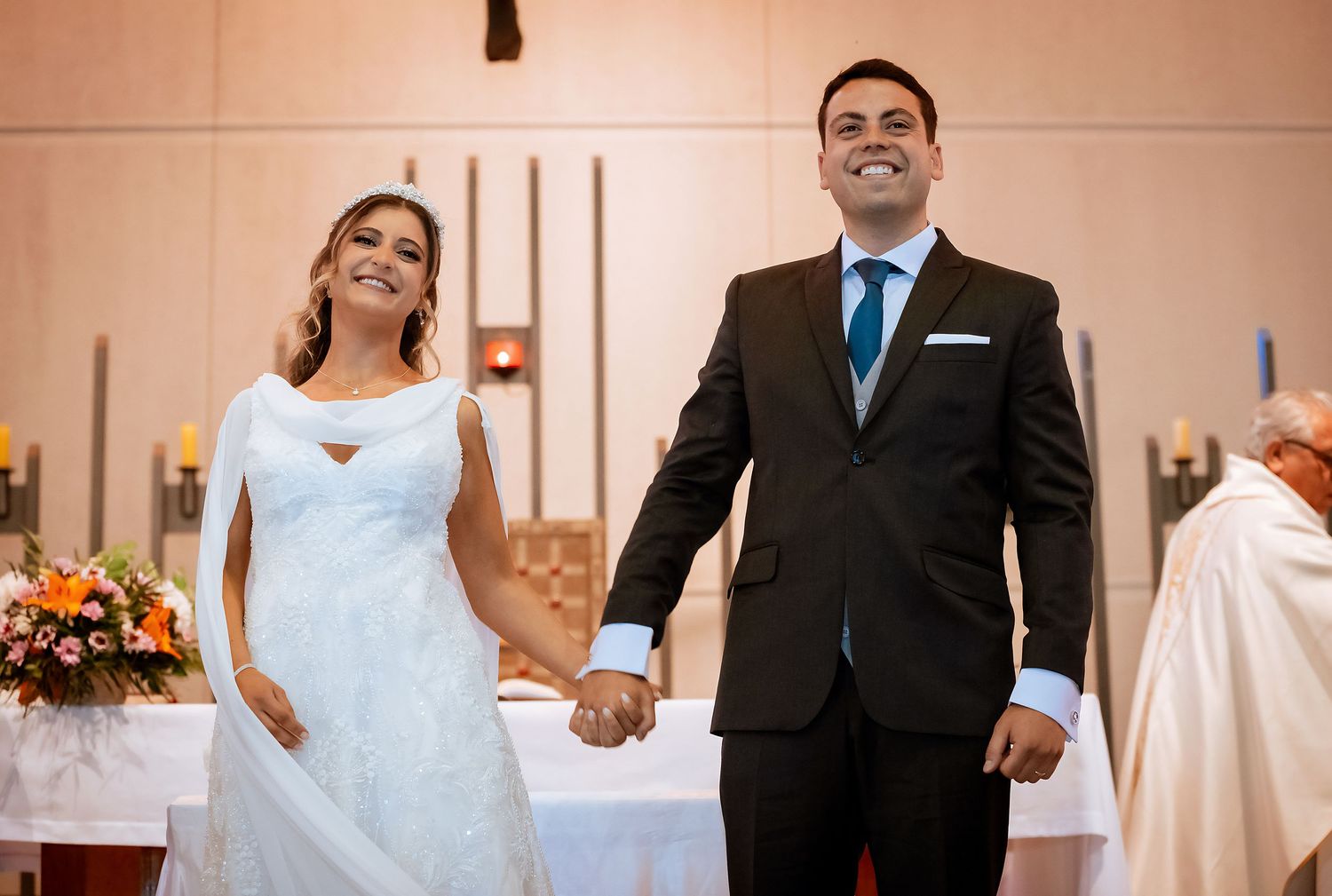 Bride and groom holding hands and smiling at church altar after exchanging wedding vows.