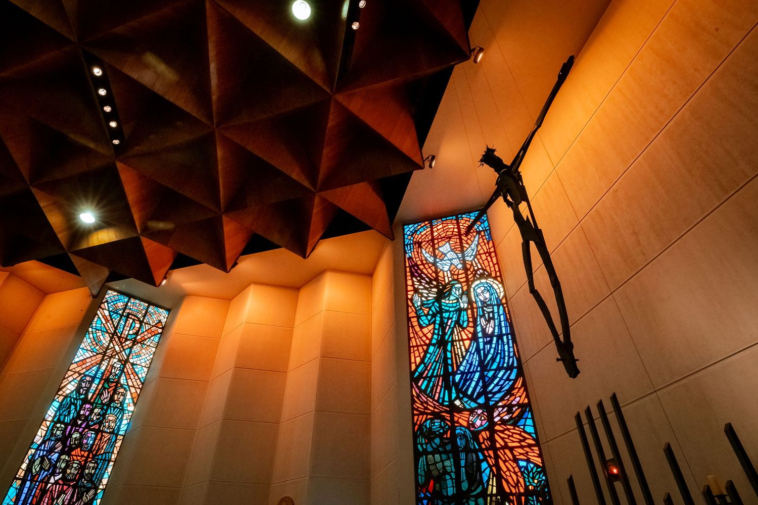 Stunning modern church interior with colorful stained glass windows, geometric ceiling, and a large crucifix.