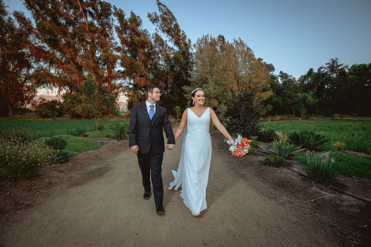 Bride and groom strolling hand in hand along a scenic garden path at golden hour.
