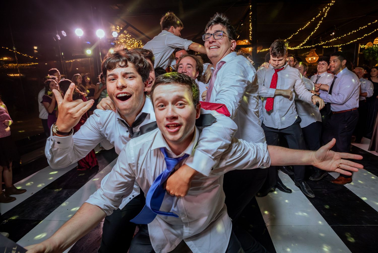 Young groomsmen laugh and pose together on wedding reception dance floor.