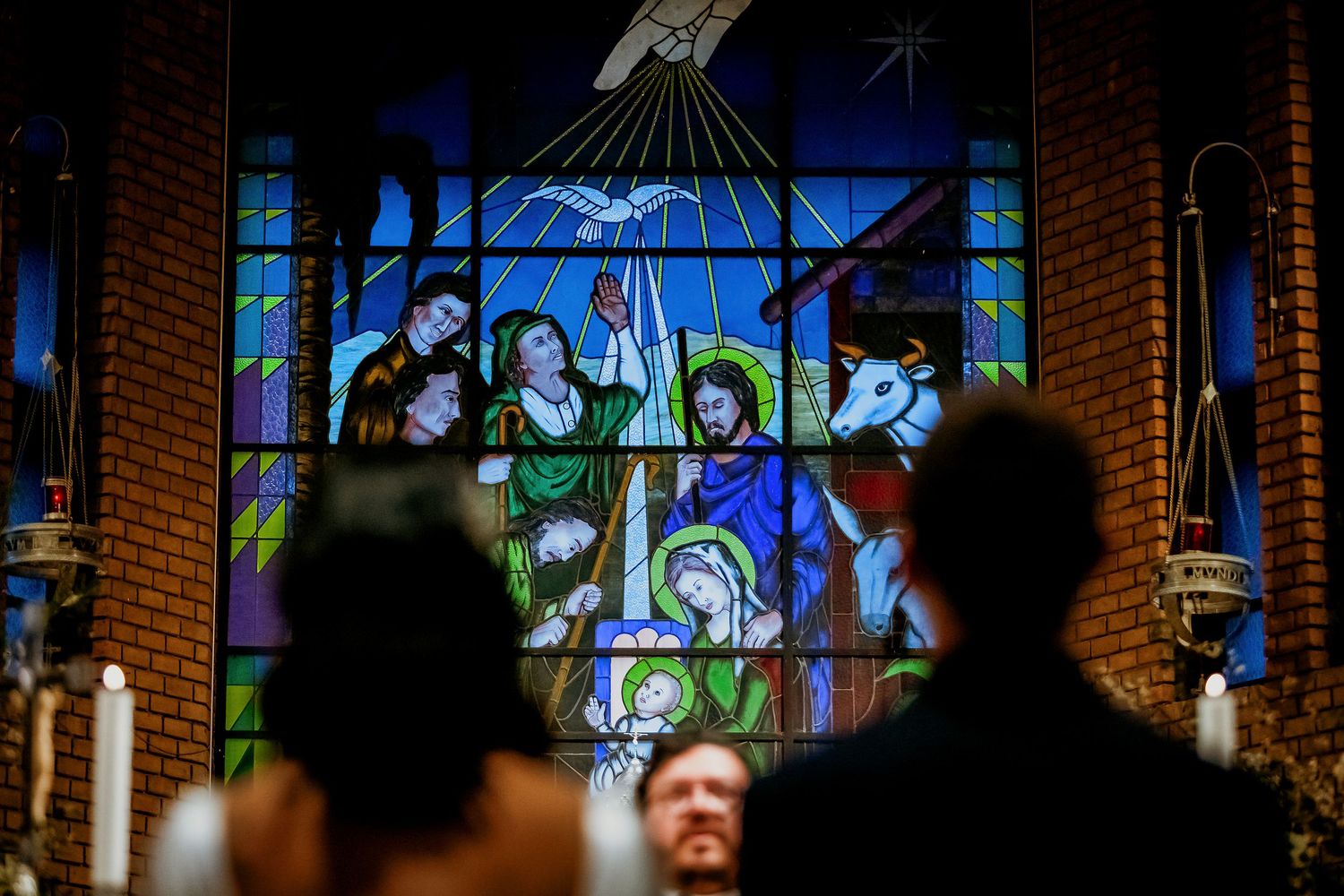 Wedding ceremony with couple before a vibrant stained glass nativity window in a brick church.
