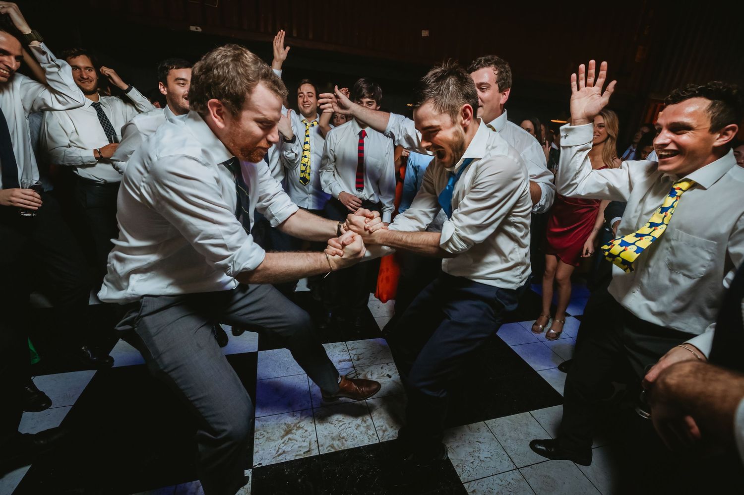 Men in dress shirts dancing energetically at a wedding reception party on the dance floor.