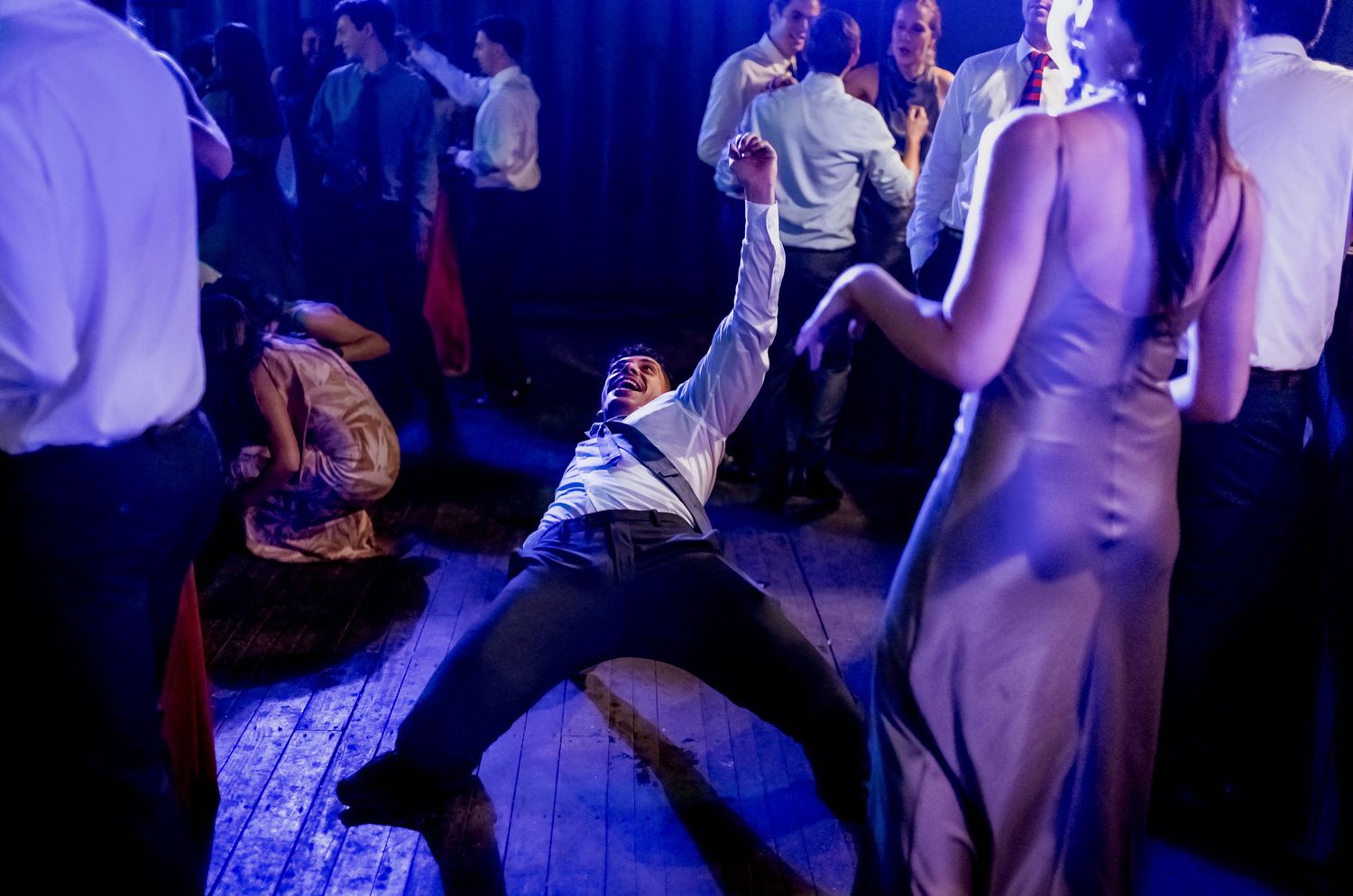 Man dramatically leaning back on dance floor at lively party with guests dancing in blue-lit venue.