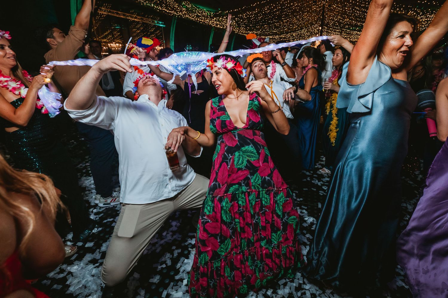 Guests in vibrant outfits dance and kneel on foam-covered dance floor at a lively wedding celebration.