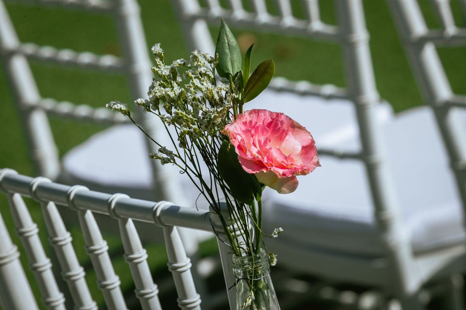 Pink rose and baby's breath floral decoration attached to white chiavari ceremony chair.