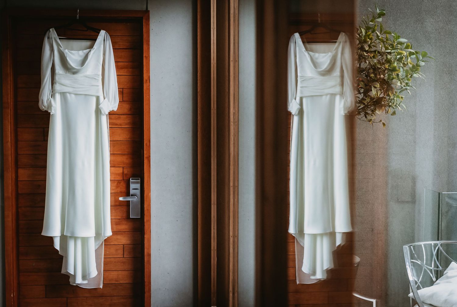 Two elegant white wedding dresses hanging on a wooden door in a bridal suite before the ceremony.
