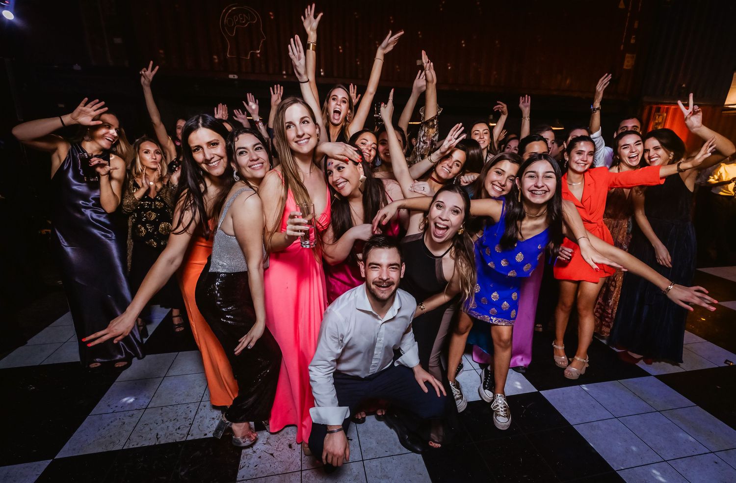 Large group of elegantly dressed partygoers celebrating on a dance floor, posing with raised arms and smiles.