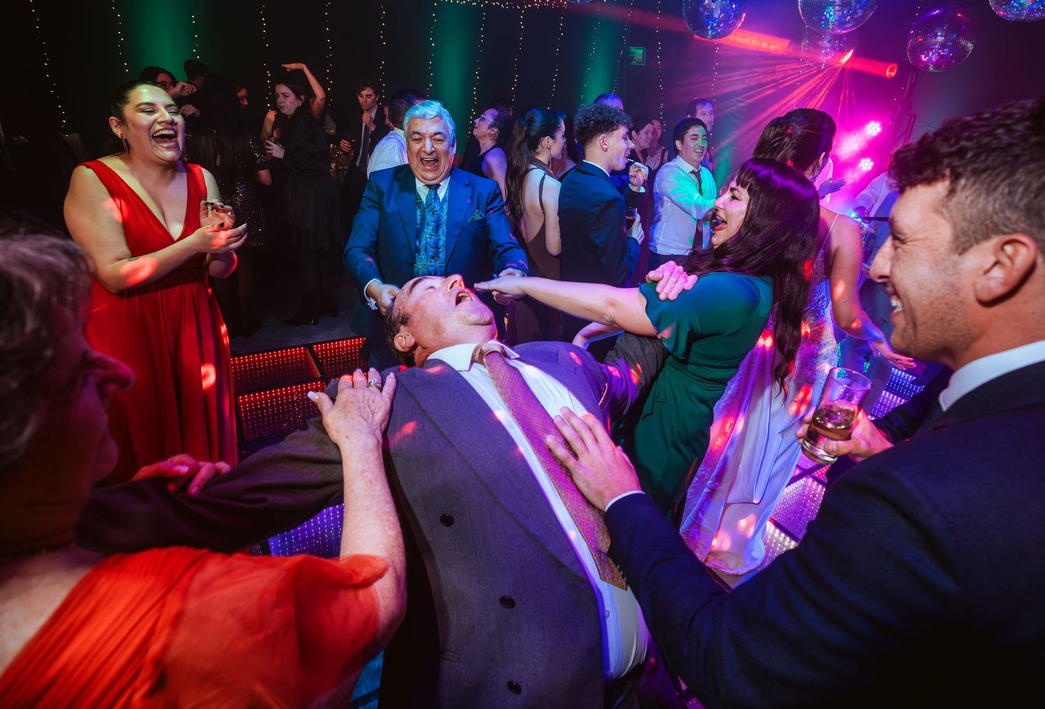Guests dancing and celebrating at a lively wedding reception party under colorful disco lights.