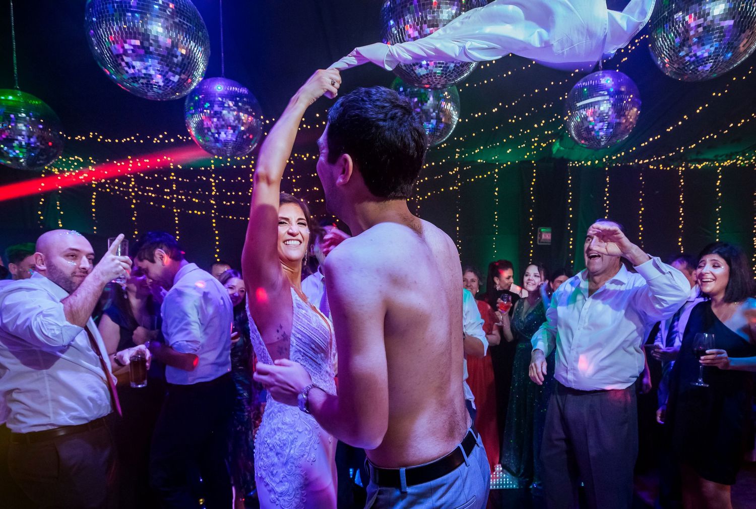 Couple dancing at a lively party with disco balls, laser lights, and guests celebrating in the background.