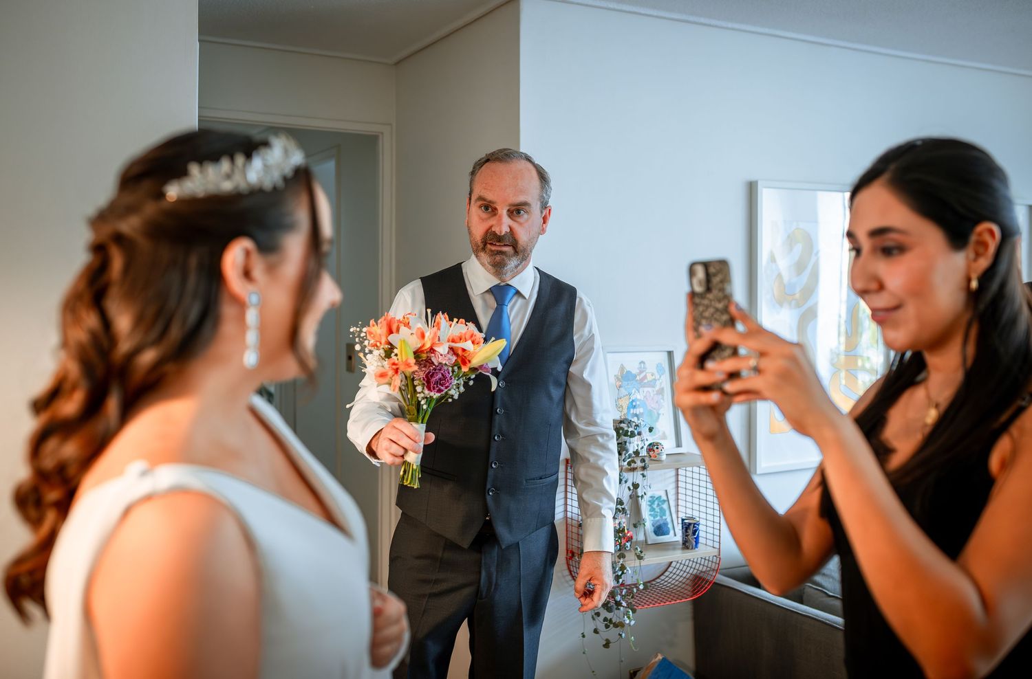 Groom presents colorful bouquet to bride as bridesmaid captures the moment on phone.