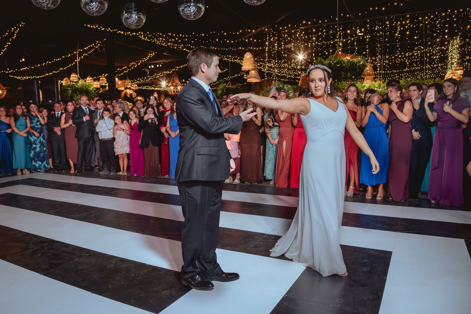 Couple shares first dance on black and white checkered floor at wedding reception.