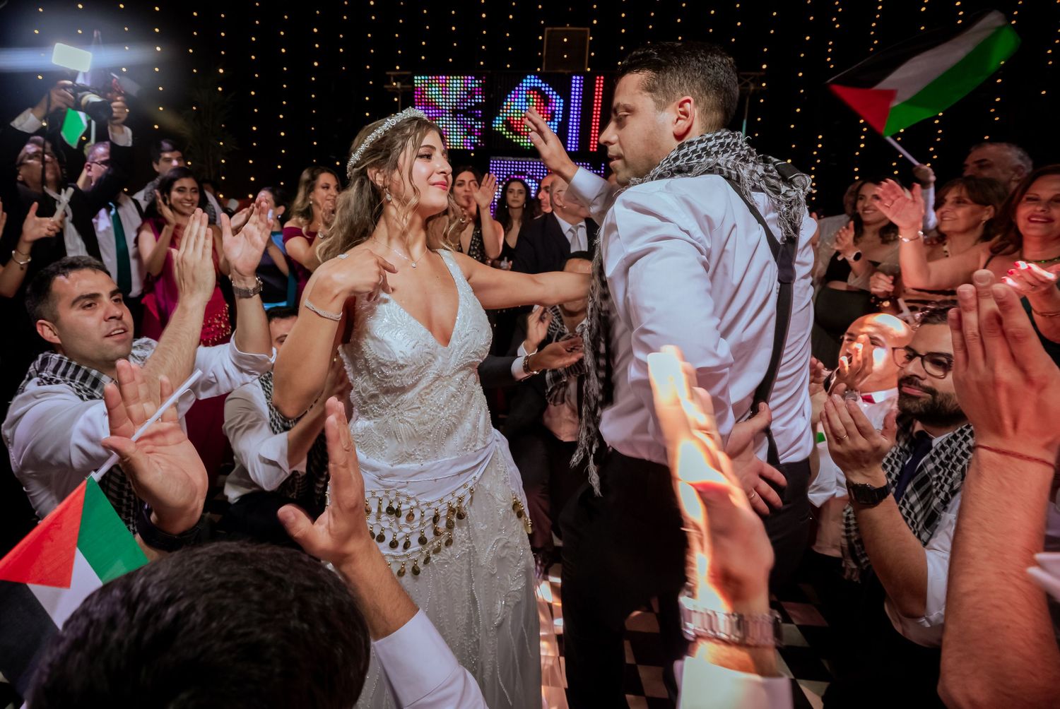 Bride and groom sharing a dance surrounded by cheering guests at a wedding celebration.