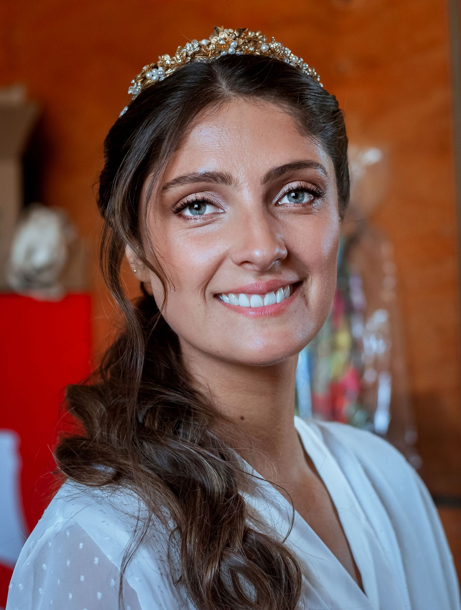 Beautiful bride smiling warmly wearing a sparkling tiara and white robe during wedding preparations.