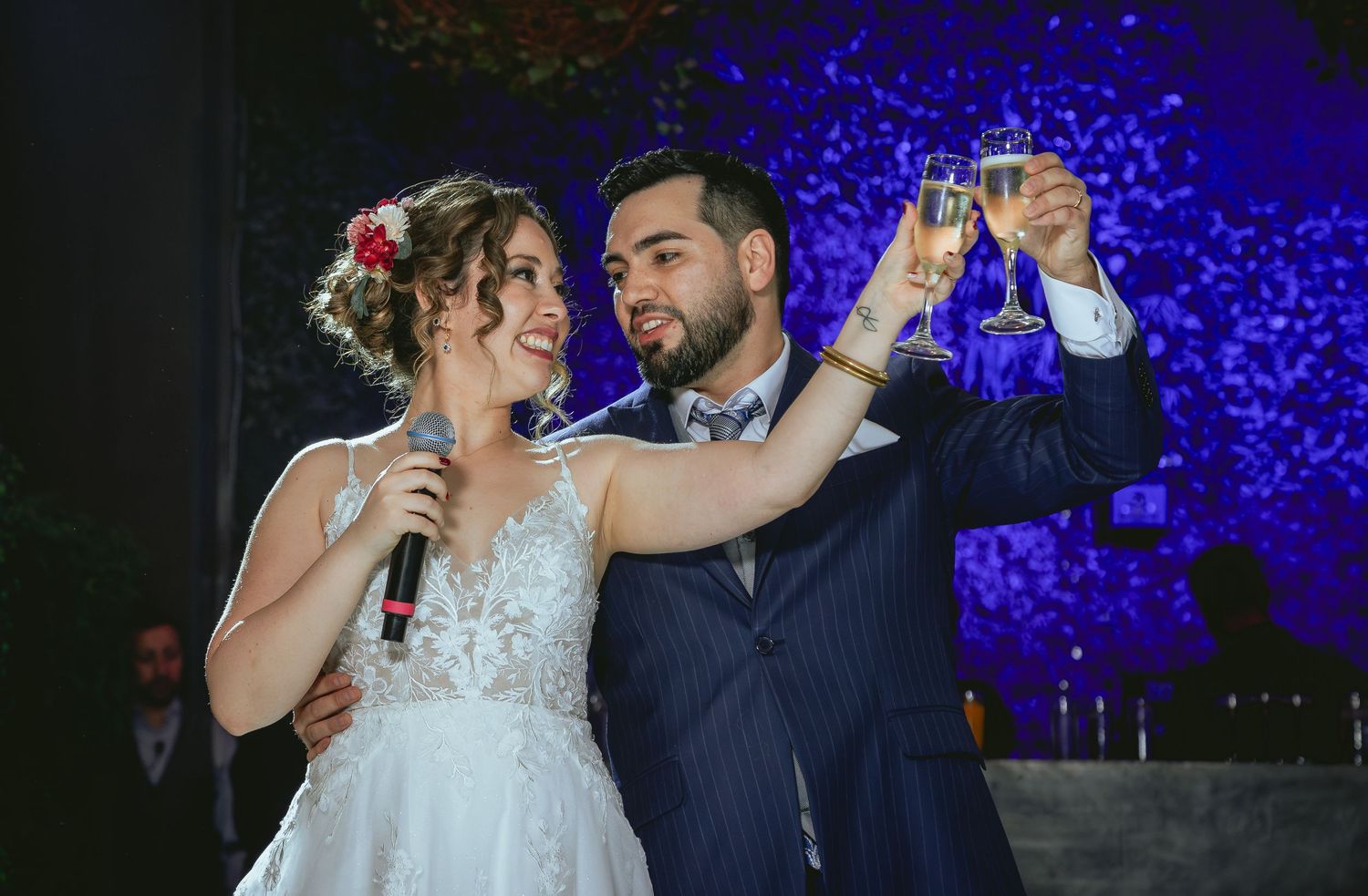 Newlyweds toast with champagne glasses while bride holds microphone at wedding reception celebration.