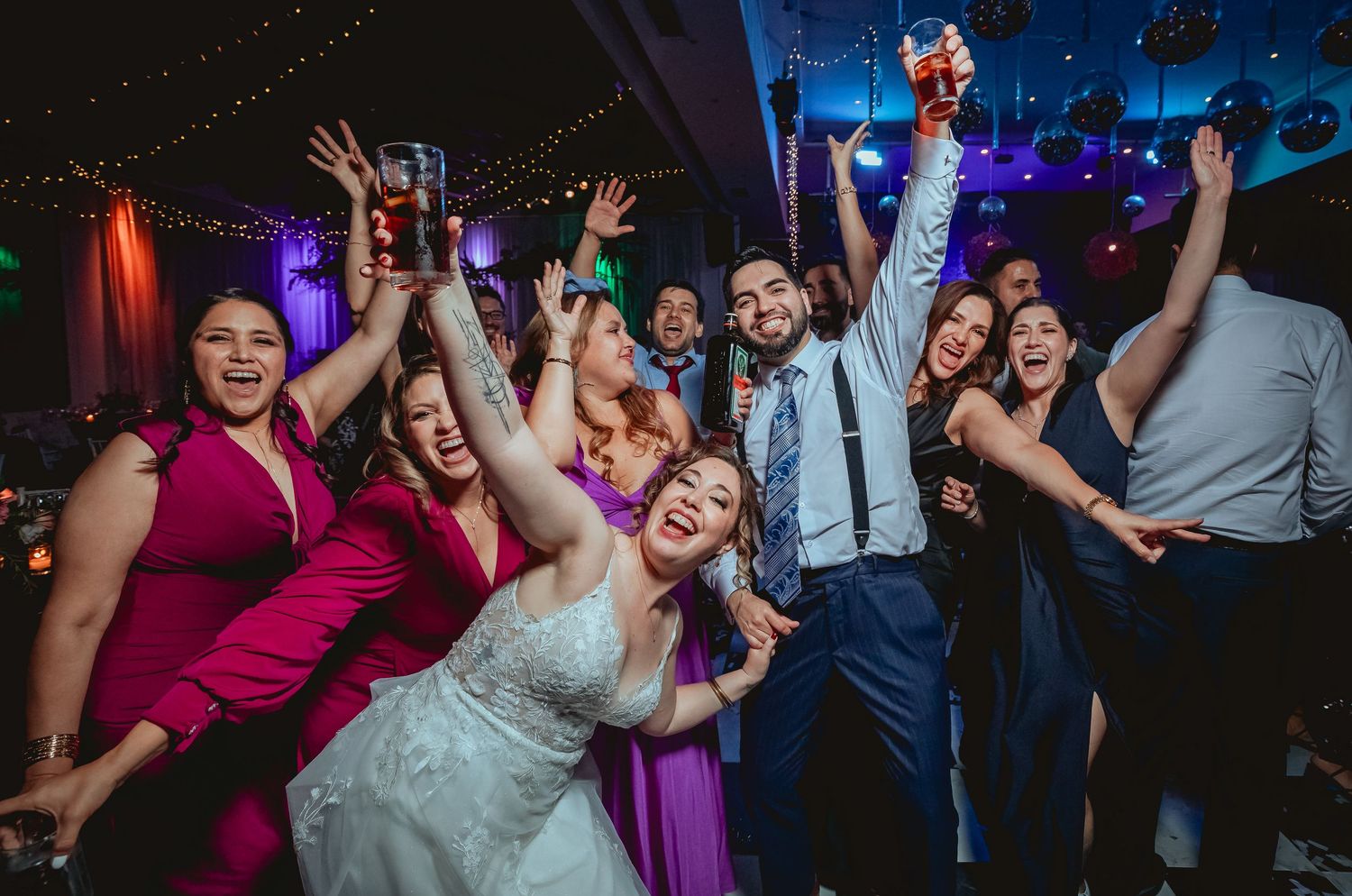 Bride and groom celebrate with wedding guests on colorful dance floor at reception.
