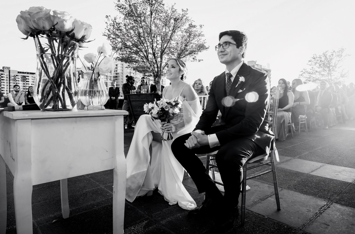 Black and white photo of bride and groom seated at outdoor wedding ceremony.