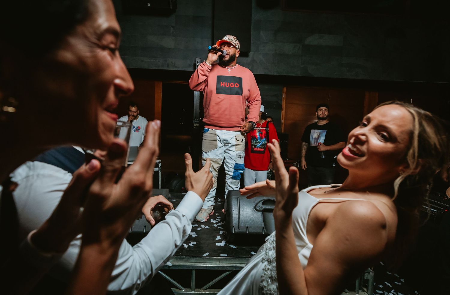 A rapper in a pink Hugo Boss hoodie performs on stage while energetic fans cheer in the foreground at a live event.