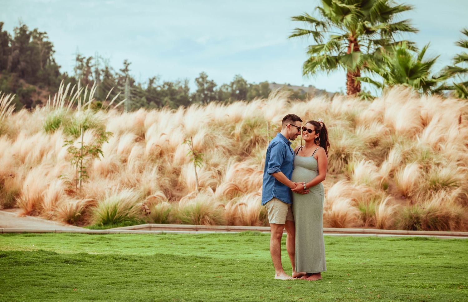 Couple embracing tenderly on green lawn with pampas grass and palm tree in sunny outdoor setting.