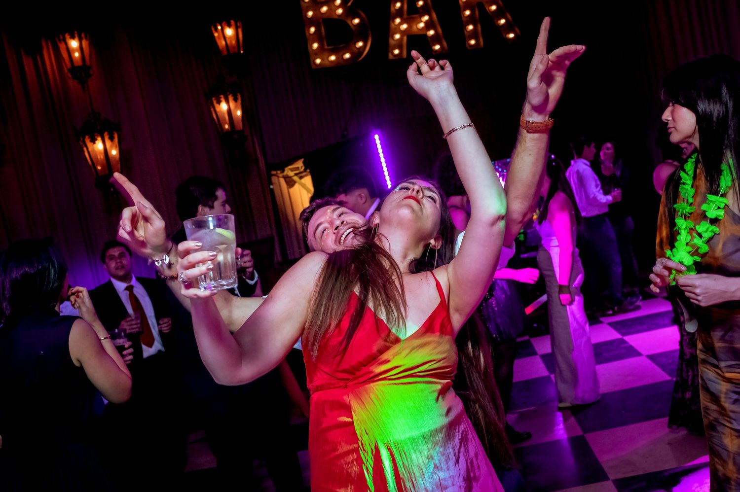 Two women dancing joyfully under colorful lights on a festive wedding reception dance floor.