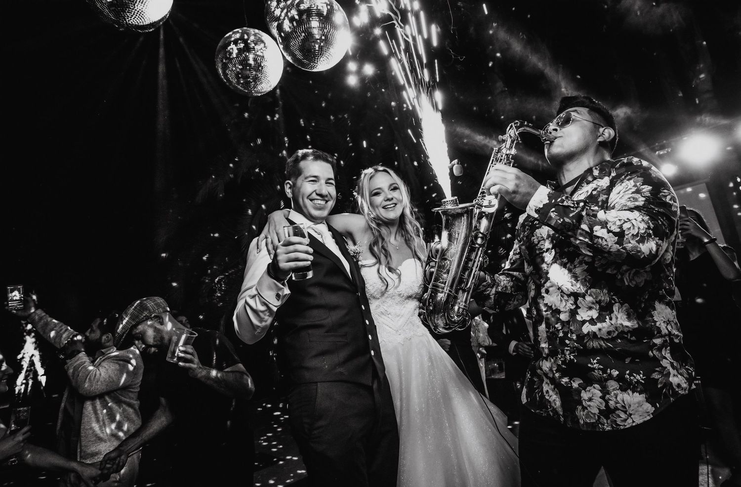 Black and white photo of smiling bride and groom with saxophonist at wedding.