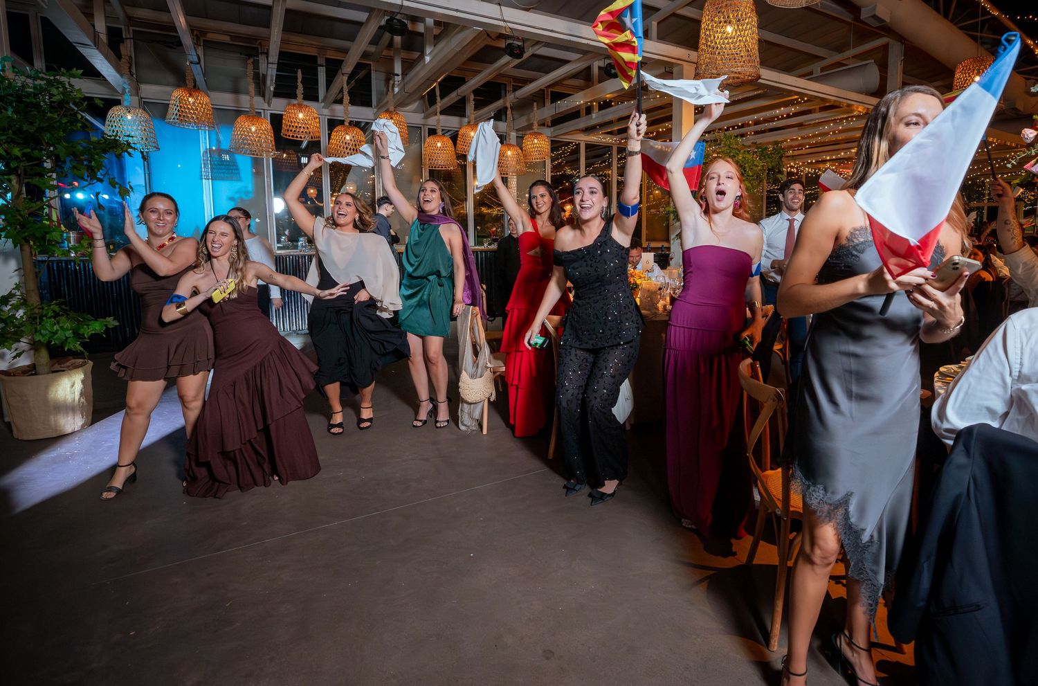 Energetic wedding guests dancing and celebrating on dance floor waving flags at lively reception party.