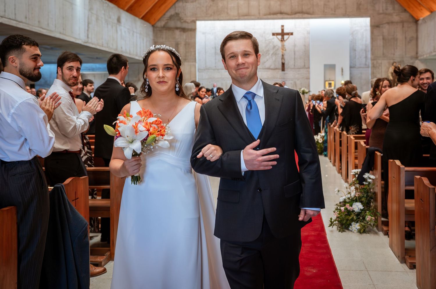 Smiling bride with bouquet and groom walk arm-in-arm down church aisle after wedding.