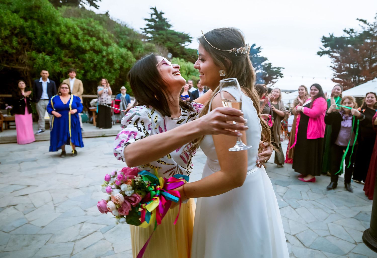 Bride and guest share a joyful embrace after bouquet toss at outdoor wedding reception.