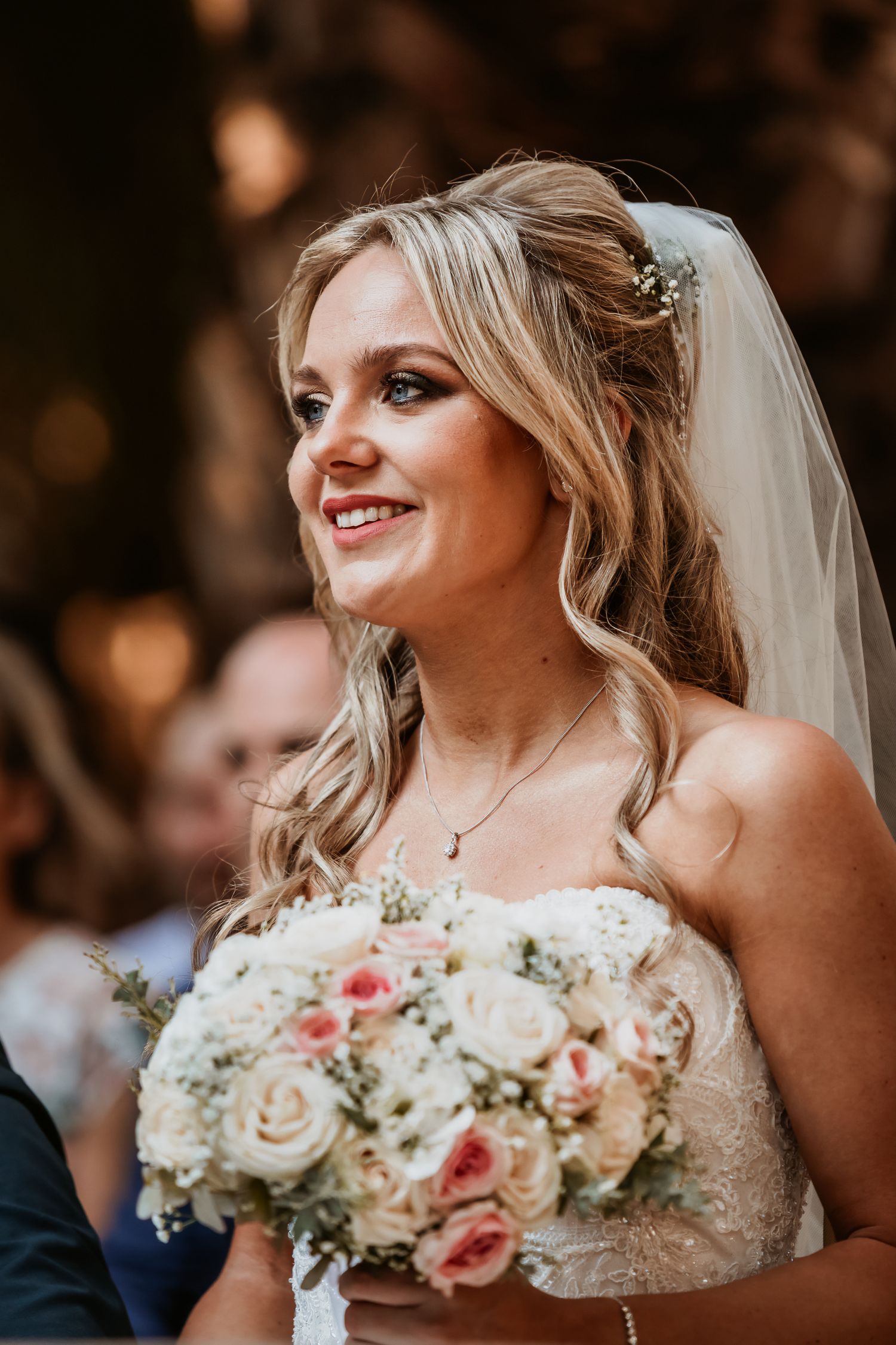 Beautiful smiling bride with wavy blonde hair holding pink and white rose bouquet.
