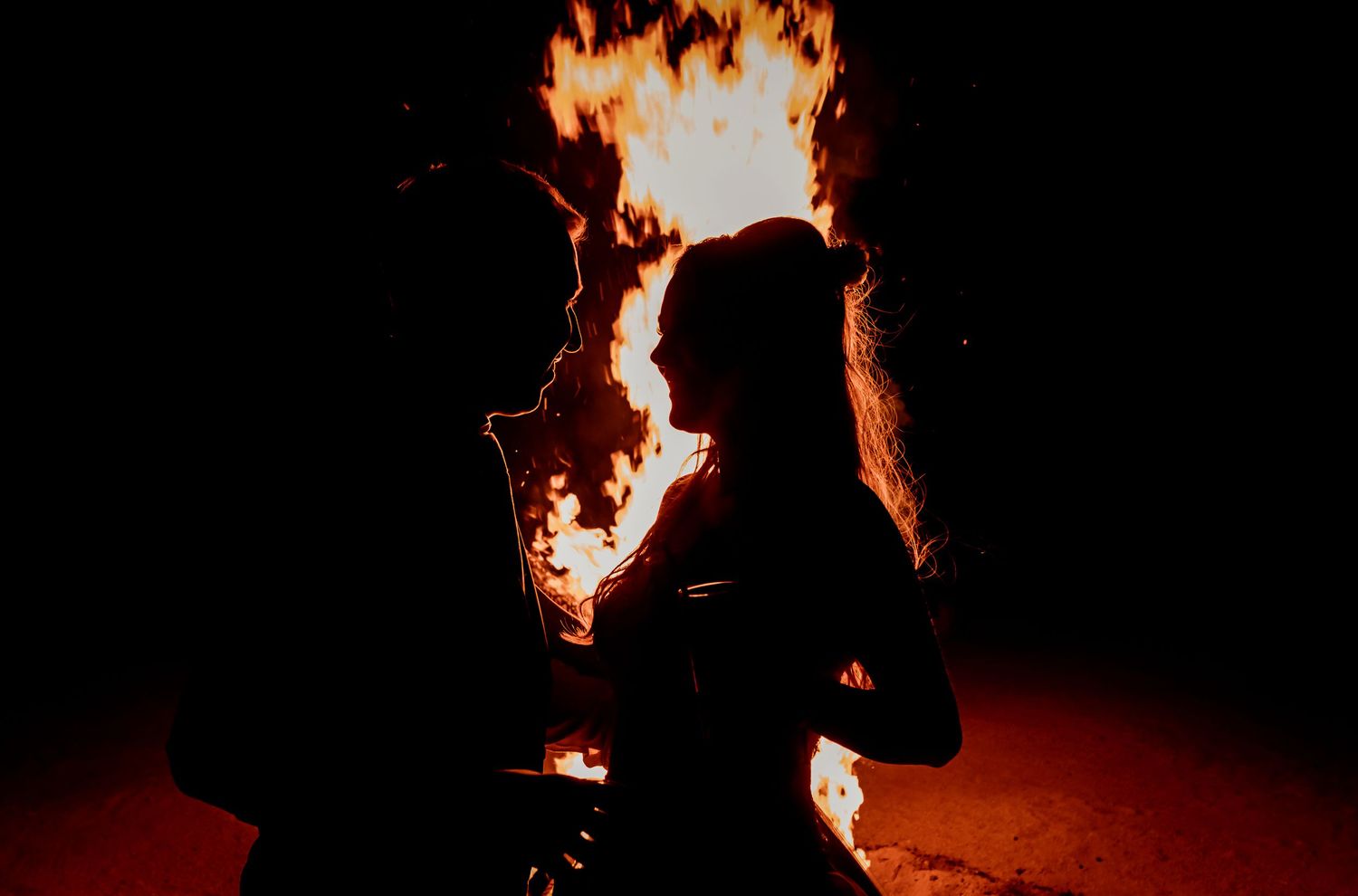 Romantic silhouette of couple standing before dramatic fire display at night.