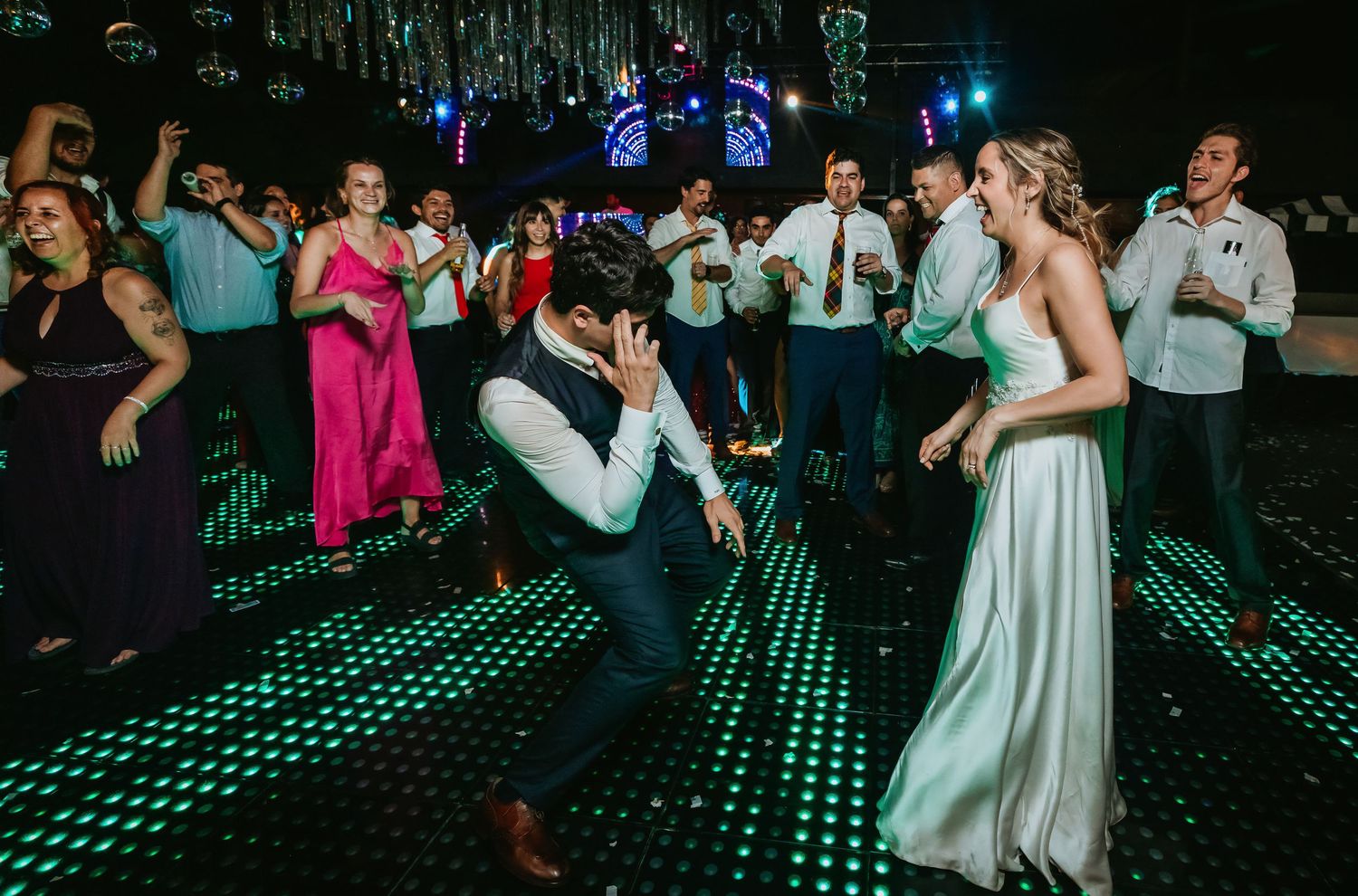 Bride in white gown and groom dancing joyfully with guests at a wedding reception.