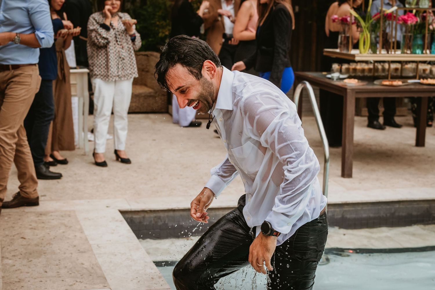 Man in wet white shirt laughing while splashing in a pool at an outdoor party gathering.