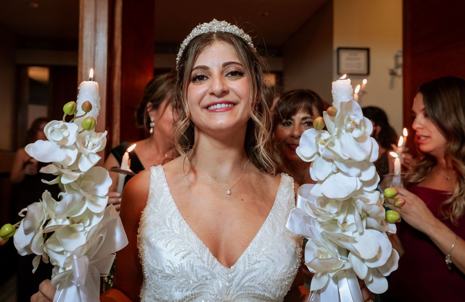 Smiling bride holding elegant candles adorned with white orchids at her wedding ceremony.