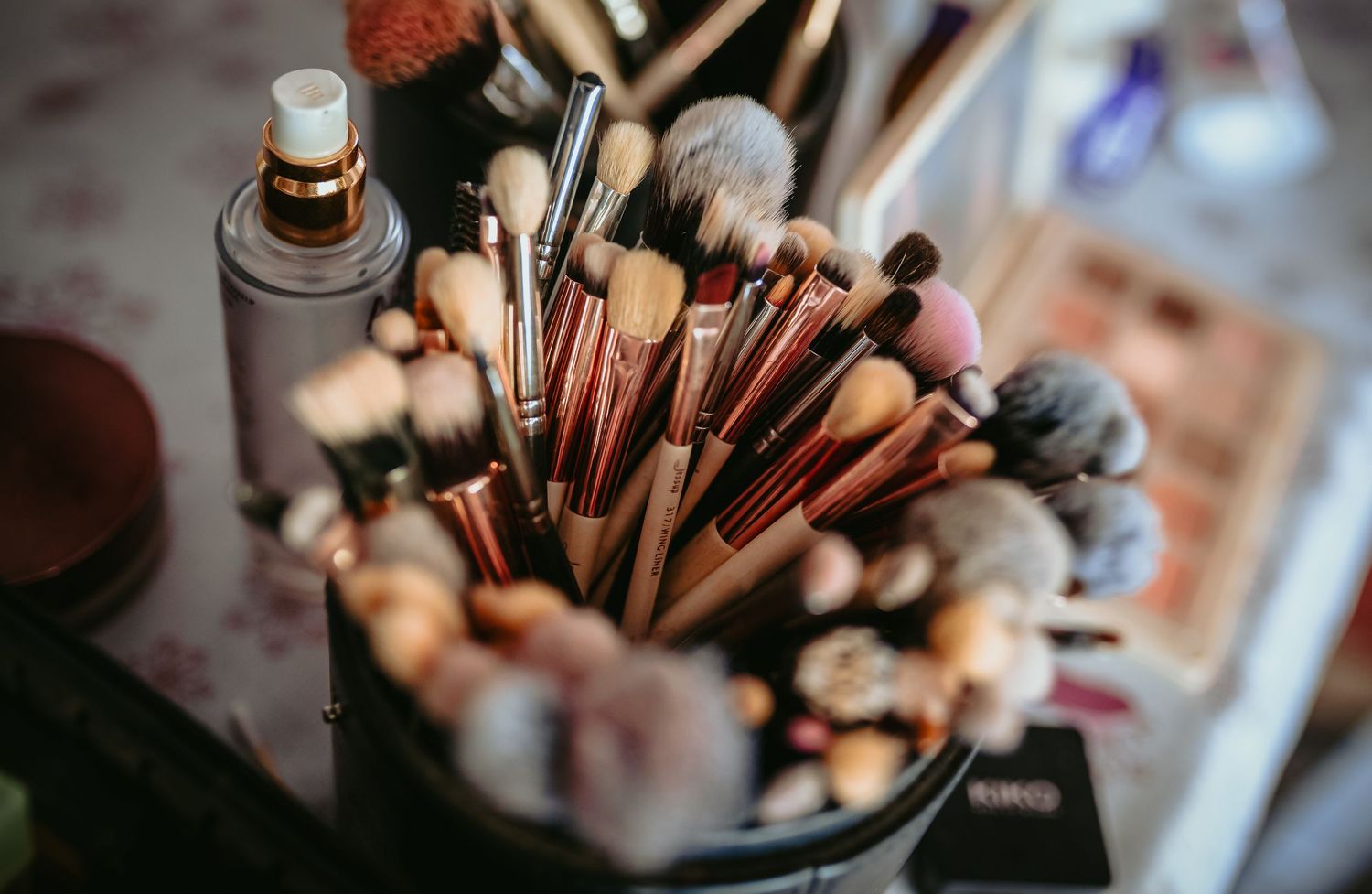 Collection of professional makeup brushes with rose gold handles in a holder on a vanity.