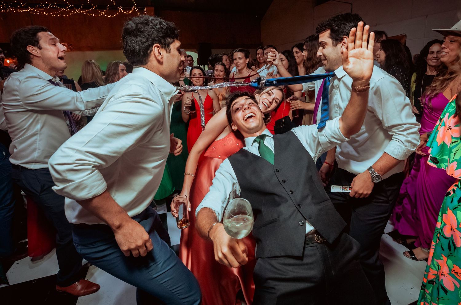 Excited wedding guests celebrate on dance floor, laughing and dancing together at lively reception party.