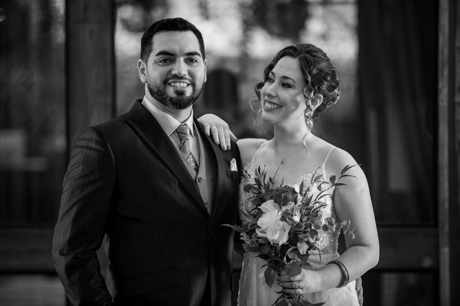 Black and white wedding portrait of smiling bride and groom posing together with a bouquet.
