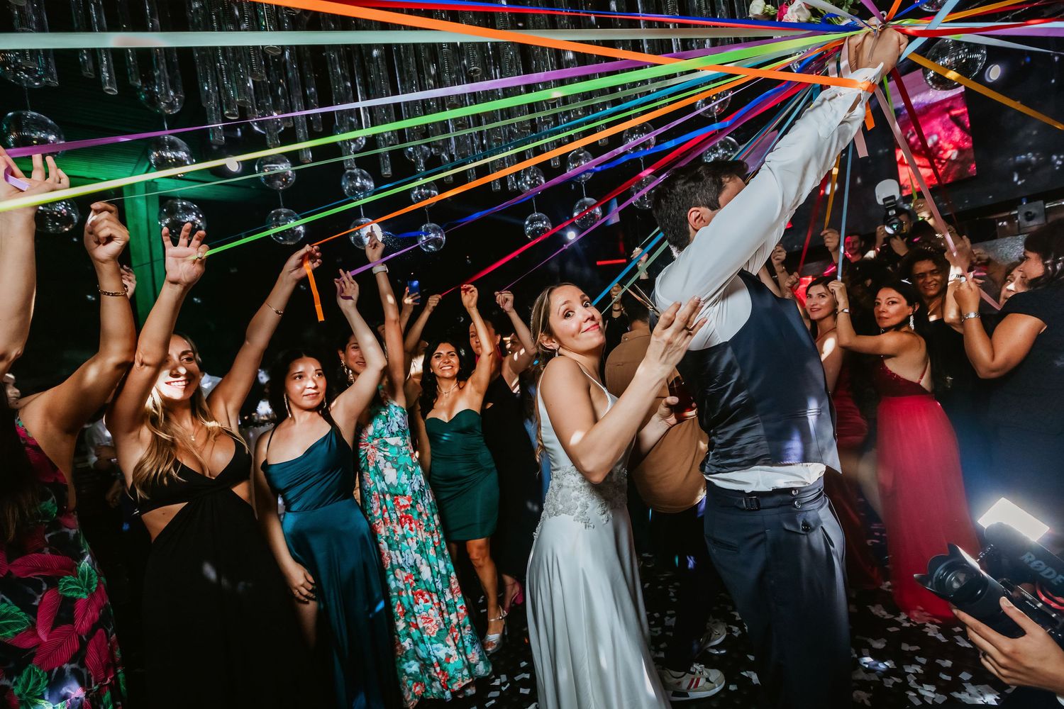 Bride and groom dancing with colorful streamers among wedding guests.