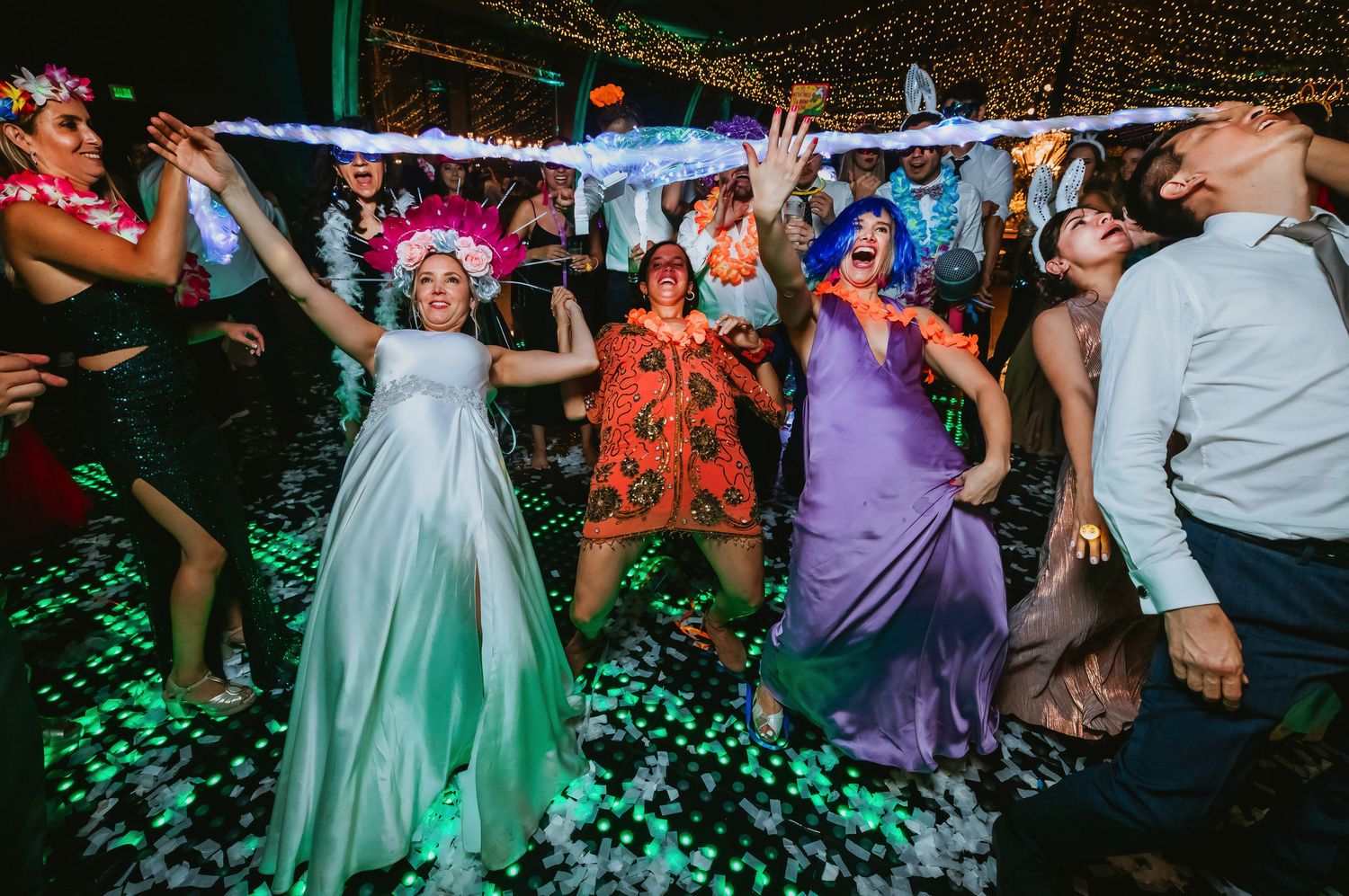 Guests dancing energetically at a colorful wedding reception with green dance floor lighting and festive accessories.