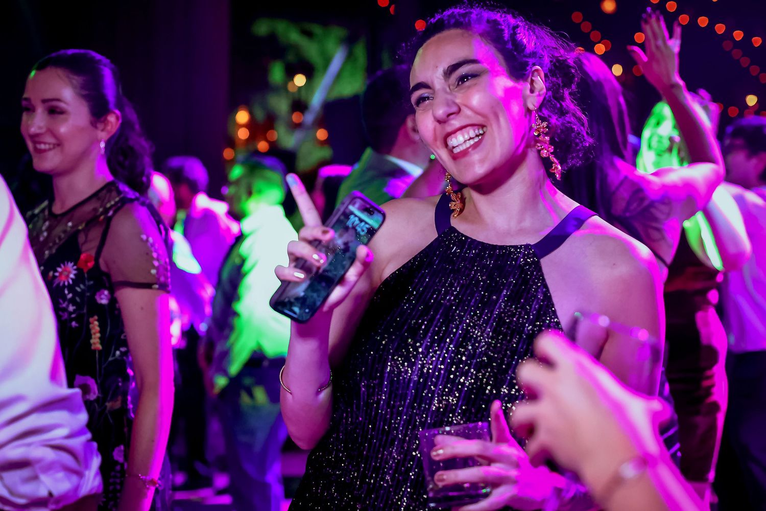 Smiling woman in black sequin dress enjoys a lively wedding reception party with colorful neon lights.